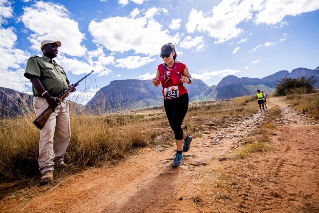 Runner competing in the Big Five Marathon, passing a ranger looking out for wild animals